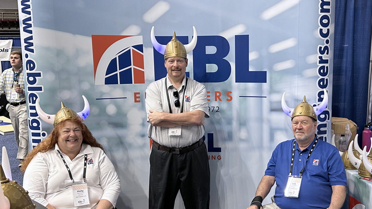 Picture of Holly, Tony and Bob in front of EBL booth wearing viking helmets